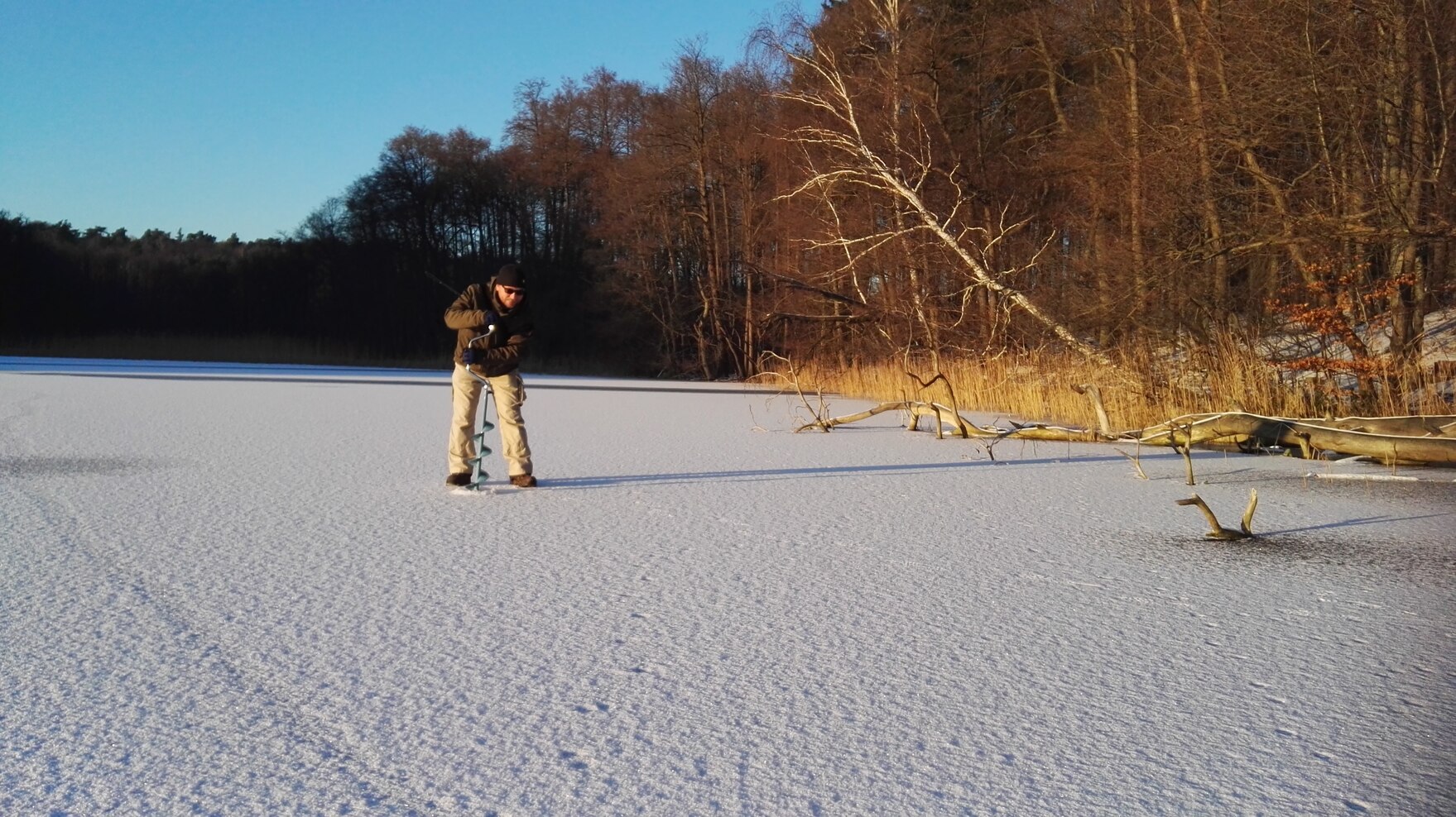 Vorbereitung zum Eisangeln: Ein Mann bohrt ein Loch in die Eisdecke des zugefrorenen Sees.