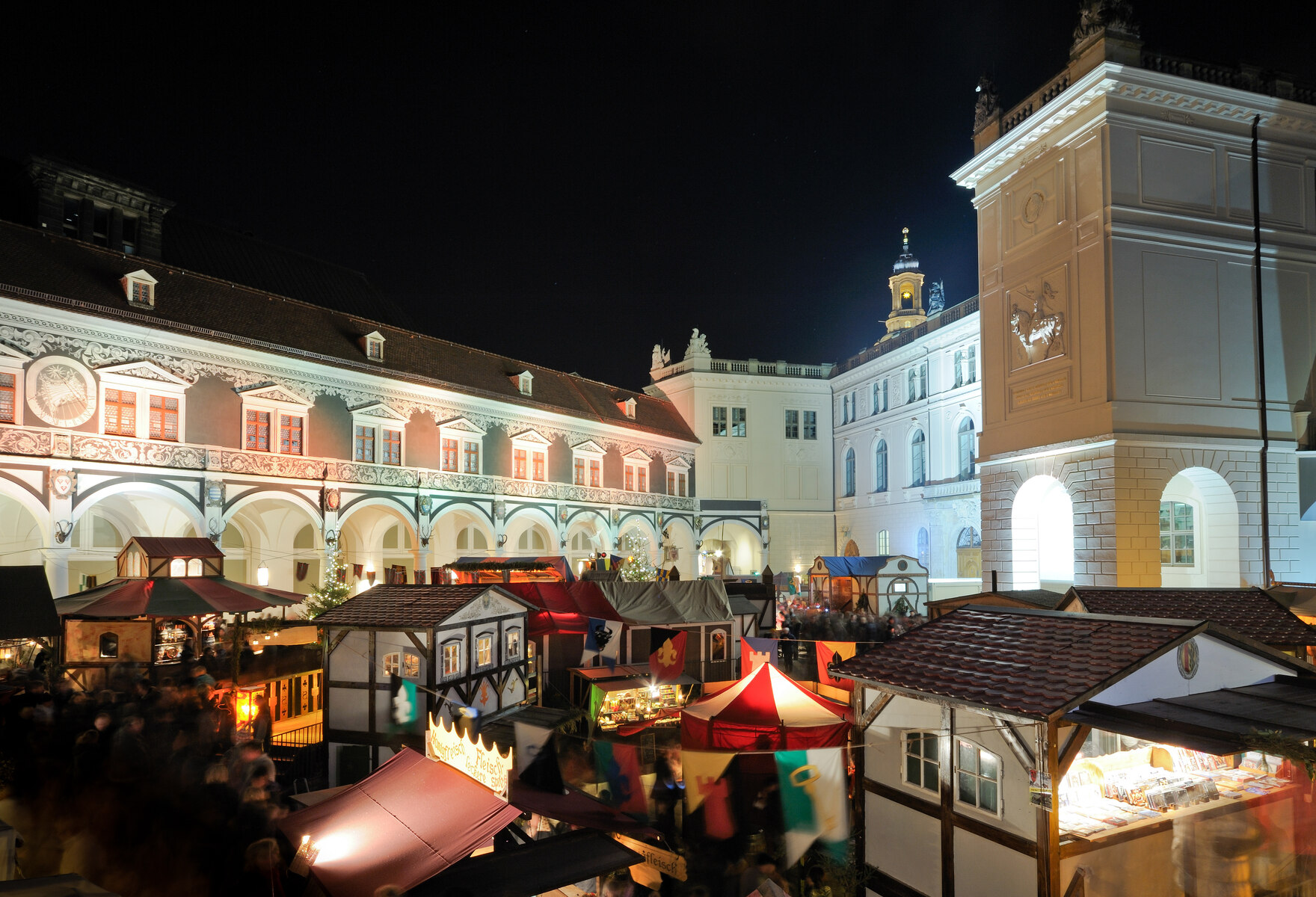 Blick über die individuell gestalteten Marktbuden auf dem Weihnachtsmarkt. Er ist umgeben von den historischen Gebäuden des Residenzschlosses.