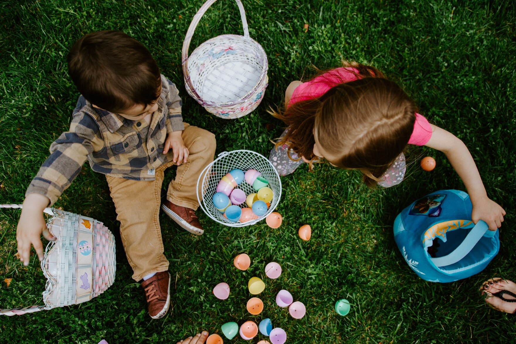 Zwei Kinder sitzen umgeben von Ostereiern auf einer Wiese. 