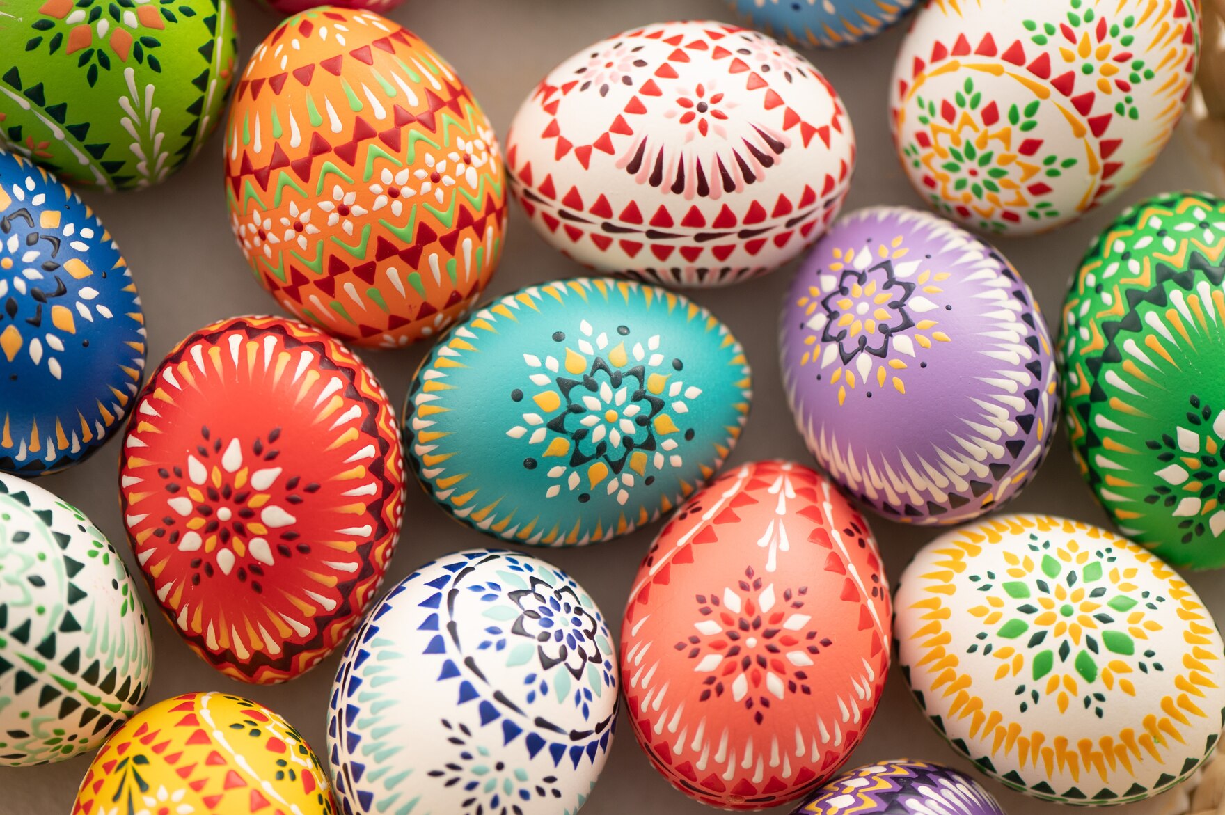 Many colourful Easter eggs are lying on a flat surface. 