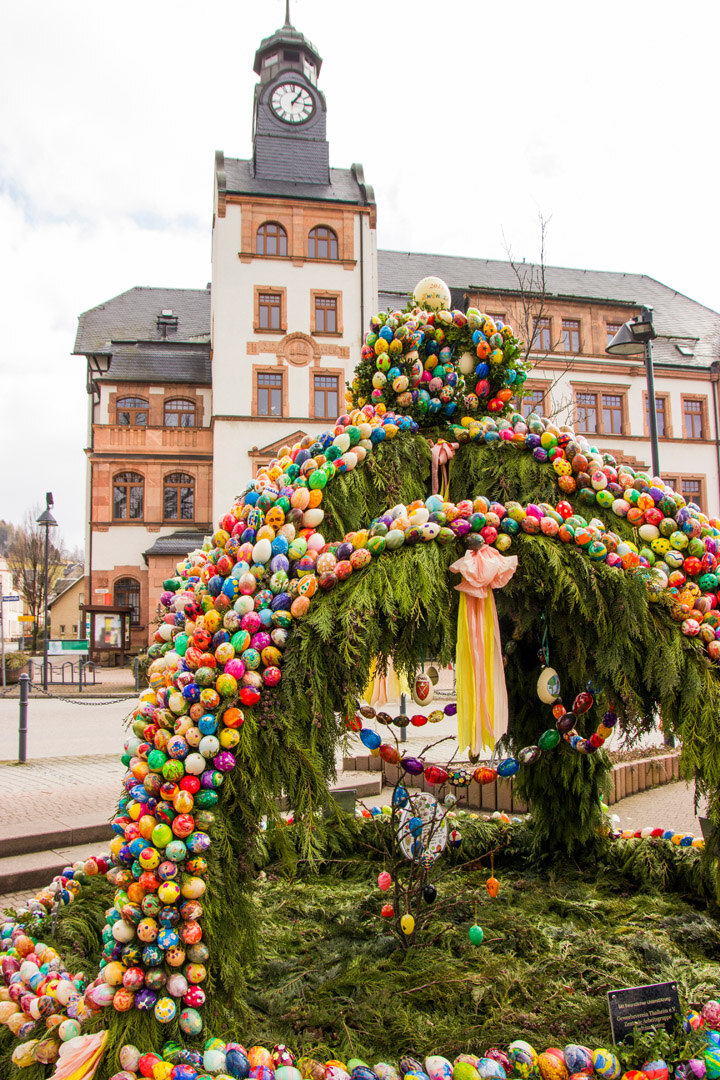 An einem Brunnen hängen viele bunte Ostereier. 