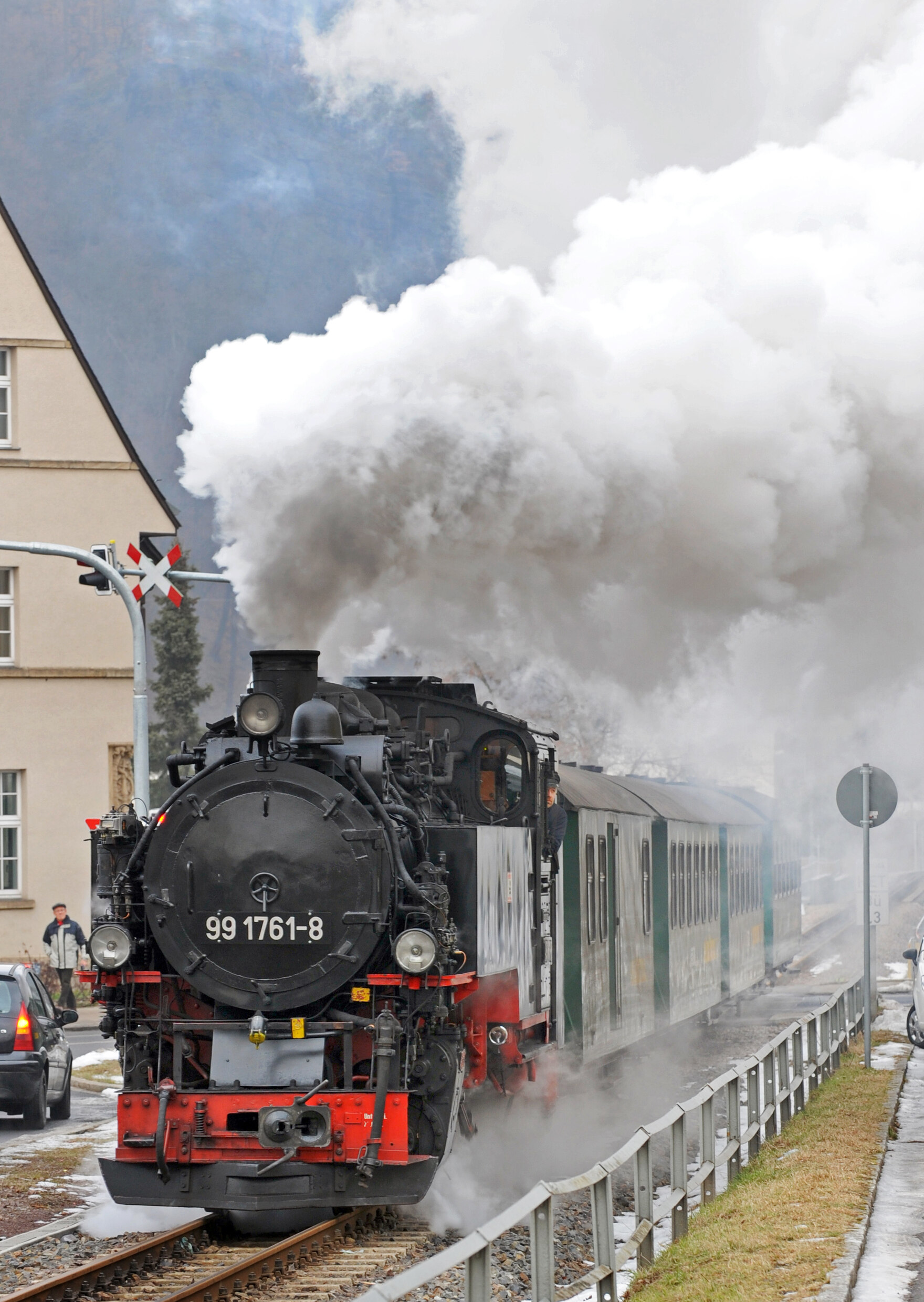 Dampfende Lok fährt über einen Bahnübergang.